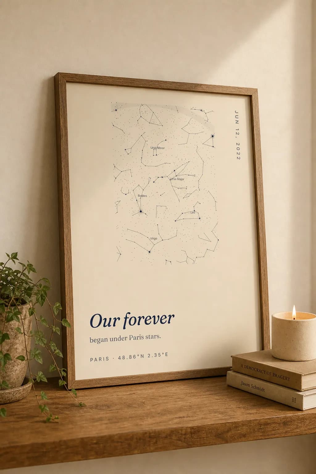 A framed cream-vintage SkyWhen star map print leaning on a shelf beside a candle and a plant